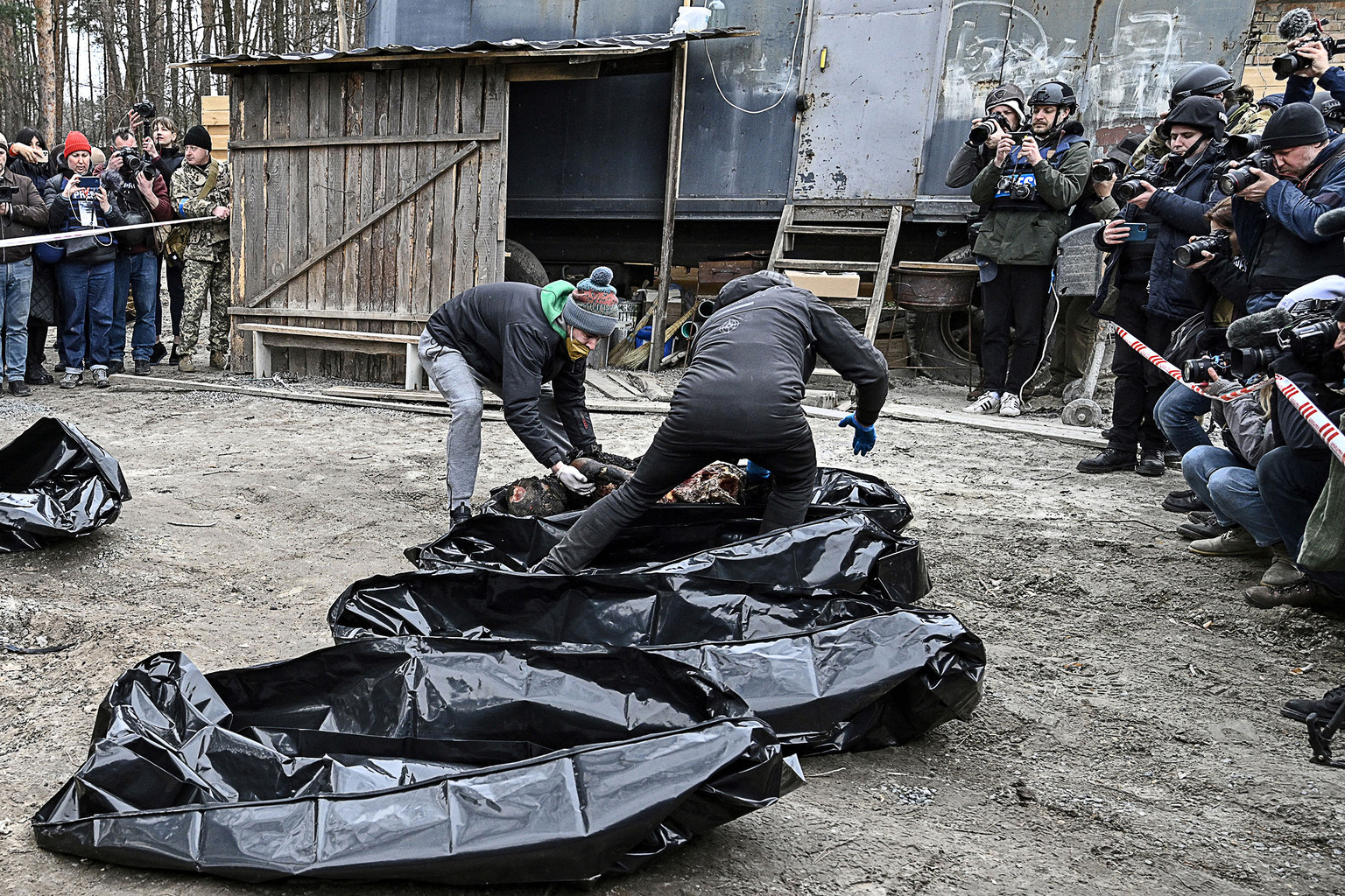 Rendőrök és önkéntesek rakják zsákokba az elhunytakat az Ukrajnai Bucsában 2022. április 5-én riporterek kamerái előtt #moszkvater